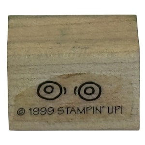 May include: A rectangular wooden rubber stamp featuring a black ink illustration of two circular eyes. The wood block has the text "© 1999 STAMPIN' UP!" printed in black ink on the front surface, indicating the brand and the year of production.