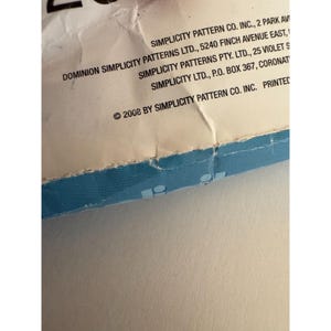 May include: A white paper sewing pattern envelope with a blue bottom edge. The text reads Simplicity Pattern Co. Inc., 2 Park Ave, Dominion Simplicity Patterns Ltd., 5240 Finch Avenue East, Simplicity Patterns Pty. Ltd., 25 Violet St, and 2008 by Simplicity.