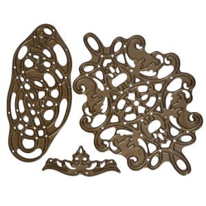 Peut inclure: Quatre découpes en métal de couleur bronze de différentes formes ornées. Les motifs comprennent un ovale avec un motif complexe, un grand motif floral et un petit élément décoratif. Ces découpes sont probablement utilisées pour l'artisanat.