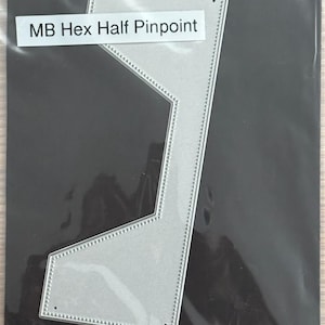 Może przedstawiać: Srebrna metalowa wykrojnik o unikalnym geometrycznym kształcie z napisem "MB Hex Half Pinpoint". Wykrojnik ma kropkowaną obwódkę i jest umieszczony na ciemnym tle. Ten przedmiot jest prawdopodobnie używany do rękodzieła lub scrapbookingu.