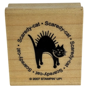 May include: A square wooden rubber stamp featuring a black silhouette of an arched-back cat with spiky fur. The text Scaredy-cat is printed in a circle around the cat, and the text 2007 STAMPIN' UP! is printed at the bottom of the wood block.