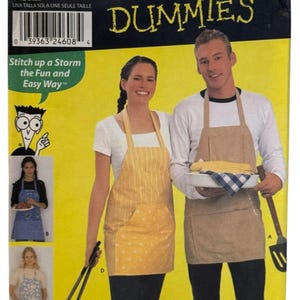 May include: Simplicity apron sewing pattern for dummies. The package features two people wearing aprons. The woman is wearing a yellow apron with white polka dots and the man is wearing a tan apron. The package has the text "Sewing Patterns for Dummies".