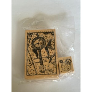 May include: Two wooden stamps with black ink designs. One stamp features a vintage illustration of a compass and celestial map with the text "Horologium Pendulum Luna". The other stamp features a design of gears.