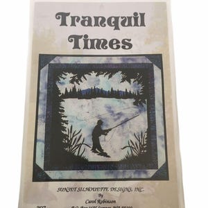 May include: A package featuring a quilt pattern with the text "Tranquil Times." The design shows a silhouette of a person fishing on a lake, surrounded by trees and reeds. The package is from Sunset Silhouette Designs, Inc.