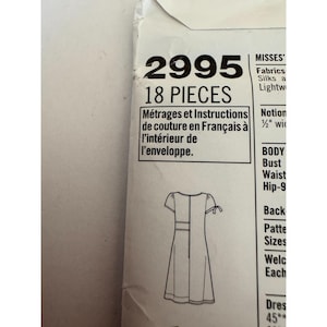May include: A white paper sewing pattern envelope labeled 2995 with 18 pieces. The front displays a black line drawing of a short-sleeved dress with tie details on the sleeves and text in English and French regarding instructions inside.