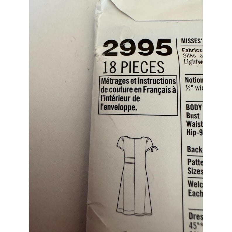 May include: A white paper sewing pattern envelope labeled 2995 with 18 pieces. The front displays a black line drawing of a short-sleeved dress with tie details on the sleeves and text in English and French regarding instructions inside.