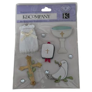 May include: A package of K&Company dimensional stickers. The stickers include a white baptism gown with a bow, a chalice, a cross, a bible, a dove with an olive branch, and clear gems. The package reads "DIMENSIONAL STICKERS".