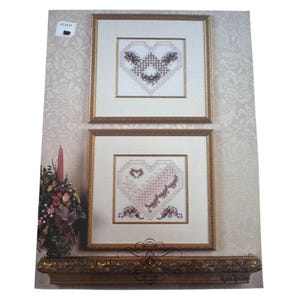 May include: Two framed cross-stitch heart designs. The top heart features a dark floral pattern, while the bottom heart has a pink and red floral design. The frames are gold, and the background is a floral pattern. The text "Heart of My Heart" is visible.