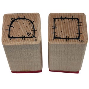 May include: Two wooden stamps with red bases. One stamp features a half-circle design with a dotted border and two hearts. The other stamp has a square design with a dotted border and cross marks at each corner. Both stamps have a copyright symbol.