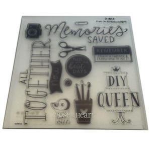 Può includere: Set di timbri trasparenti con varie immagini e testo a tema scrapbook. Include una fotocamera, forbici, pennelli e le parole "Memories Saved", "DIY QUEEN" e "All Together."