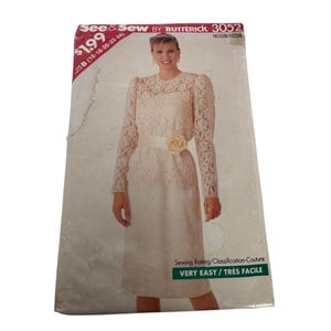 May include: A vintage Butterick sewing pattern, featuring a cream-colored dress with lace sleeves and a floral belt. The pattern includes sizes 16-24 and is rated as very easy. The pattern's cover displays the text "See & Sew by Butterick 3052".