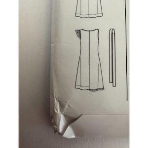 May include: A sewing pattern envelope featuring a black and white line drawing of a sleeveless dress with a ruffled shoulder detail and a separate long fabric tie. The paper envelope is off-white and shows visible creasing and folding at the corner.