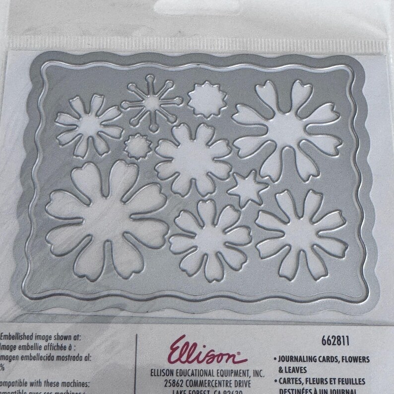 Op de afbeelding: Een zilverkleurige metalen snijmal met een geschulpte rechthoekige rand en diverse bloem- en bladvormen uitgesneden in het midden. De verpakking bevat de tekst Ellison, 662811 en Journaling Cards, Flowers & Leaves.