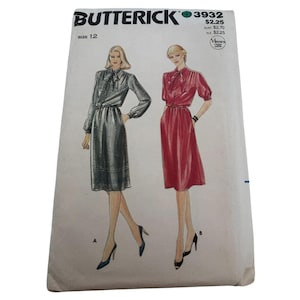 Op de afbeelding: Vintage naaipatroon voor een jurk met een strik aan de hals. Het patroon is voor maat 12 en is van Butterick patroonnummer 3932. Het patroon toont twee verschillende versies van de jurk, een in grijs en een in rood.