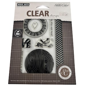 May include: A set of Hero Arts and Studio Calico clear stamps in original packaging. The set includes a circular floral frame, a heart, the word LOVE, a bird on a branch, a wood grain circle, a chevron border, and the text you are my ha.