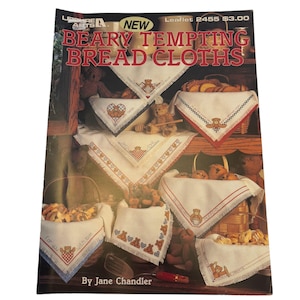 Peut inclure: Une brochure intitulée "BEARY TEMPTING BREAD CLOTHS" par Jane Chandler. La couverture présente des images de torchons brodés avec des motifs d'ours en peluche. Les torchons sont blancs avec des accents rouges, bleus et marron. Des paniers de pain et des ours en peluche sont également présentés.