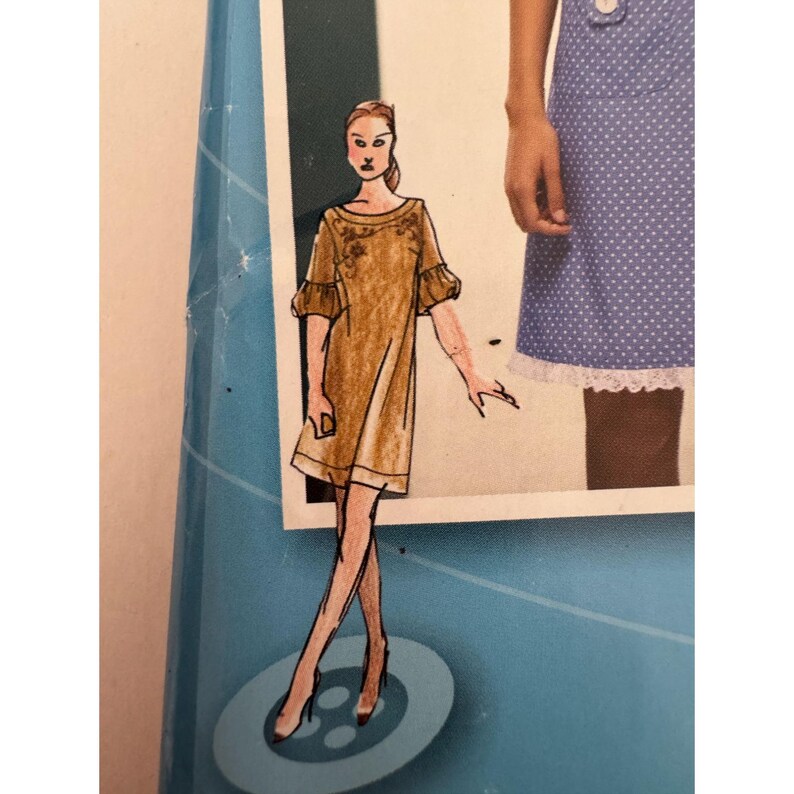 May include: A fashion illustration of a tan dress with short, ruffled sleeves and delicate floral embroidery around the neckline. The dress is depicted on a figure standing on a circular base, positioned next to a blue and white polka dot garment.