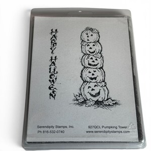 May include: A clear plastic storage case containing a rubber stamp sheet with a black ink illustration of a vertical stack of five jack-o'-lanterns and the text "HAPPY HALLOWEEN" written vertically. The label includes "Serendipity Stamps, Inc."