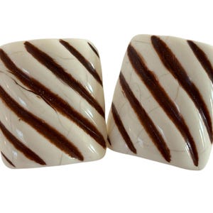 May include: Pair of square earrings with a cream-colored base and diagonal brown stripes. The earrings have a glossy finish and a slightly rounded shape, creating a vintage or retro aesthetic.