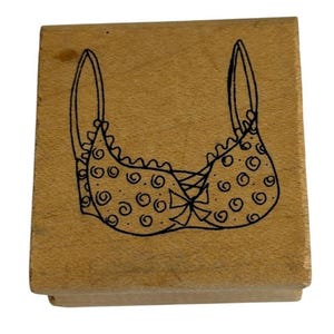 May include: A wooden stamp with a black line drawing of a bra with a polka dot pattern.