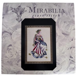 May include: Mirabilia cross stitch kit featuring a woman in a draped gown with an American flag design. The artwork is framed in gold and set against a white rose background. The kit includes the Mirabilia logo.
