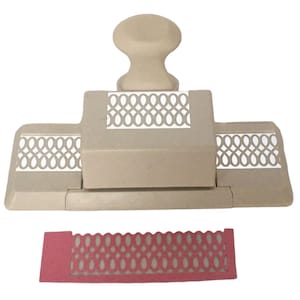 Könnte beinhalten: Ein beiger Papierstanzer mit einem dekorativen Gitterdesign. Der Stanzer ist geöffnet und ein rotes Muster des gestanzten Designs ist darunter sichtbar.
