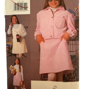 May include: A vintage Vogue for Me sewing pattern featuring a pink skirt suit and other outfits. The pattern size is 7-8-10. The cover shows a young person wearing the outfits. The Vogue logo is visible.