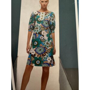 May include: A knee-length dress featuring a vibrant floral pattern in shades of teal, blue, brown, and white. The garment has three-quarter length sleeves with gathered cuffs and a central placket at the neckline adorned with a row of round buttons.