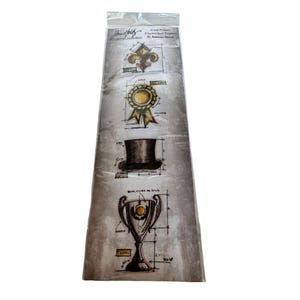 May include: A sheet of four vintage-style rubber stamps featuring a fleur-de-lis, a ribbon award, a top hat, and a trophy. The stamps are printed on a textured, gray background with black and white lines.