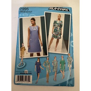 May include: A Simplicity Project Runway sewing pattern envelope 2995, size D5 4, 6, 8, 10, 12. The blue packaging displays illustrations and photographs of various dress designs, including a blue polka dot dress with white buttons and a floral print dress.