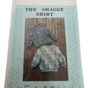 May include: A package featuring a sewing pattern for "The Shaggy Shirt" from "A Quilter's Wardrobe." The pattern cover displays two shaggy sweaters in shades of gray and blue, set against a wooden background. The package is sealed in clear plastic.