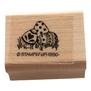 May include: Wooden stamp featuring three decorated Easter eggs in a grassy setting. One egg has a heart design, another has polka dots, and the third has an ornate pattern. The stamp includes the text "© STAMPIN' UP! 1990-".