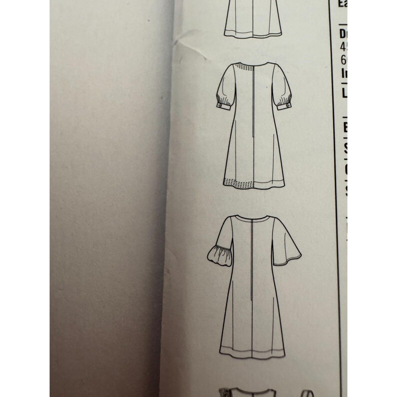 May include: A black and white sewing pattern illustration showing technical line drawings of three different dress designs. The sketches feature various sleeve lengths, including puffed sleeves with cuffs and flared sleeves, all presented on a white paper background.