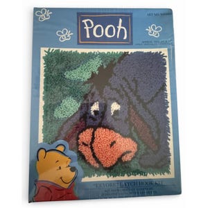 Peut inclure: Un kit de crochet à clenche Eeyore Pooh dans un emballage bleu présentant une image texturée d'Eeyore avec un nez rose sur fond vert. L'emballage affiche le texte Pooh, Eeyore Latch Hook Kit, et Art No. WP0004, avec un petit graphique de Pooh.