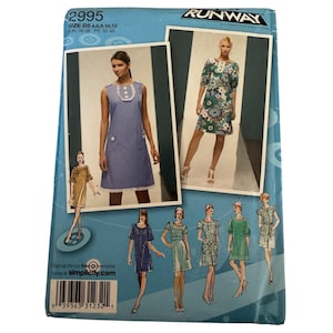 May include: A Simplicity sewing pattern envelope, number 2995, featuring Project Runway branding. The blue package displays illustrations and photographs of various dress designs, including a sleeveless blue dress with white trim and a floral print dress.