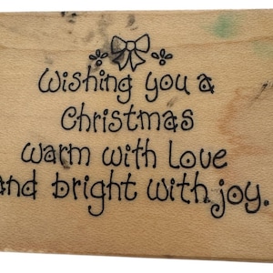 May include: A rectangular wooden sign with the message "Wishing you a Christmas warm with Love and bright with joy" in black script. A bow and floral design is at the top. The wood has a light brown color.