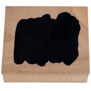 May include: A square wooden rubber stamp featuring a solid black, irregular, hand-drawn ink blot shape centered on the light brown wood block. The stamp has a flat top surface and a smooth, natural wood grain finish on all visible sides.