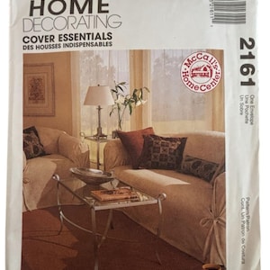 May include: A McCall's Home Decorating pattern envelope. The cover features a living room scene with a sofa, armchair, and glass-topped coffee table. The text reads "Cover Essentials" and "Des Housses Indispensables."