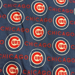 May include: Close-up of a blue fabric with a repeating pattern of Chicago Cubs logos. The logos are red and white circles with the letters "UBS" inside, and the word "CHICAGO" is written in red.
