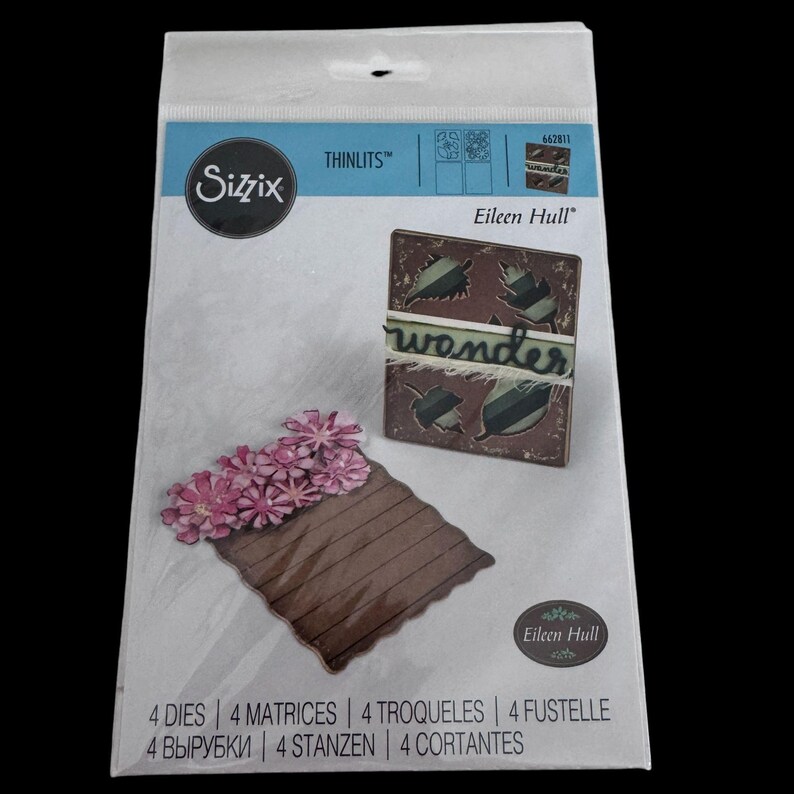 Op de afbeelding: Een Sizzix Thinlits Eileen Hull stansset in een doorzichtige plastic verpakking. De verpakking toont een bruine rechthoekige vorm met roze bloemen en een vierkant bruin frame met bladuitsnijdingen en het woord wonder in groene schrijfletters.