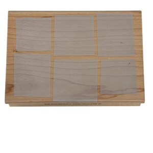 May include: A rectangular wooden block featuring six translucent, square-shaped adhesive sheets arranged in two rows. The light brown wood grain is visible beneath the sheets. Small black text is printed along the bottom edge of the wood.
