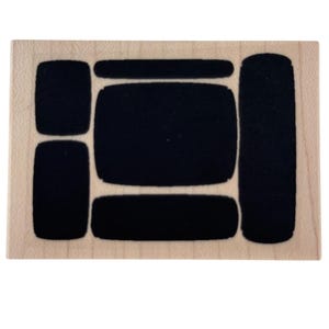 May include: A rectangular light-colored wooden block featuring a series of recessed black shapes. The design includes a large central rectangle, a long vertical rectangle on the right, and four smaller rounded rectangular shapes arranged around the center.