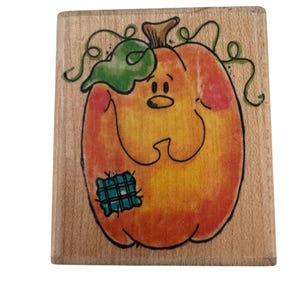 May include: A wooden stamp depicting a cartoon pumpkin with a smiling face, green leaf, and vines. The pumpkin is orange with red accents and a blue patch. Ideal for crafting and seasonal projects.