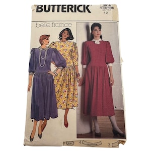 May include: A vintage Butterick sewing pattern, size 12, featuring illustrations of three dresses. The pattern is titled "Belle France" and includes a purple dress, a yellow floral dress, and a red floral dress. The pattern envelope is slightly worn.