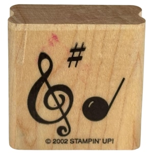 Könnte beinhalten: Ein Holzstempel mit musikalischen Symbolen: ein Violinschlüssel, ein Kreuz und eine Viertelnote. Der Stempel ist hellbraun mit schwarzen Tintendrucken. Der Text "© 2002 STAMPIN' UP!" ist unten aufgedruckt.