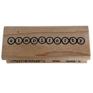 May include: A rectangular wooden rubber stamp featuring the word simplicity in lowercase letters, with each letter enclosed in a black circular outline. The base of the wood block displays the printed text 7 25718 93428 6 0704 93428 K.
