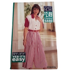 May include: A See & Sew pattern envelope 6880 for a two-piece outfit featuring a white short-sleeved shirt with a red collar and red sleeves, paired with red and white vertically striped culottes and a matching red belt. Text includes See & Sew NOW.