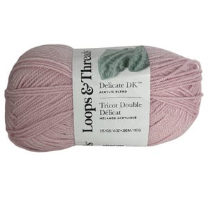 Puede incluir: Ovillo de lana rosa pálido Loops & Threads Delicate DK, mezcla acrílica. La etiqueta indica "Tricot Double Délicat" y "315 YDS/4 OZ". Ideal para proyectos de punto y ganchillo.