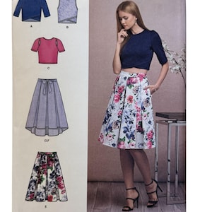 Puede incluir: Patrón de costura Simplicity con una mujer con un top corto azul marino y una falda con estampado floral. El patrón incluye ilustraciones de diferentes estilos de tops y faldas. Talla Euro 30-36.