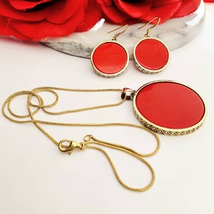 May include: A gold chain necklace with a large red pendant and matching red circle earrings. The pendant and earrings have a gold filigree design.